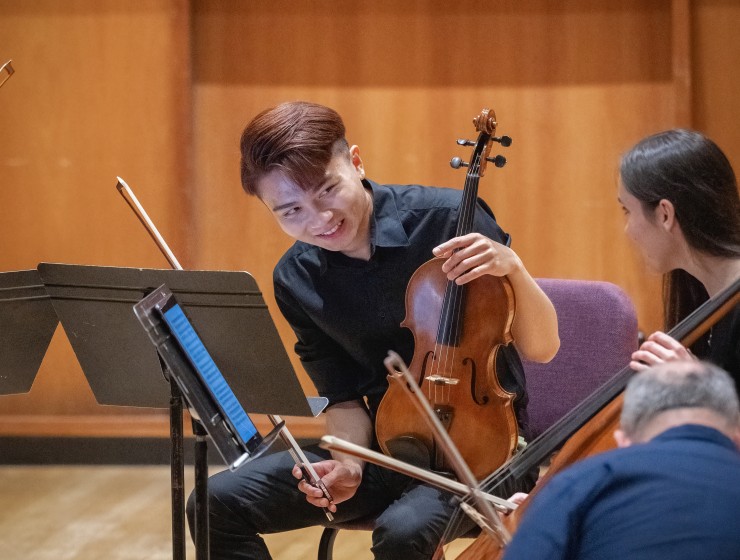 a student violist sitting on stage with their instrument smiling at their colleague