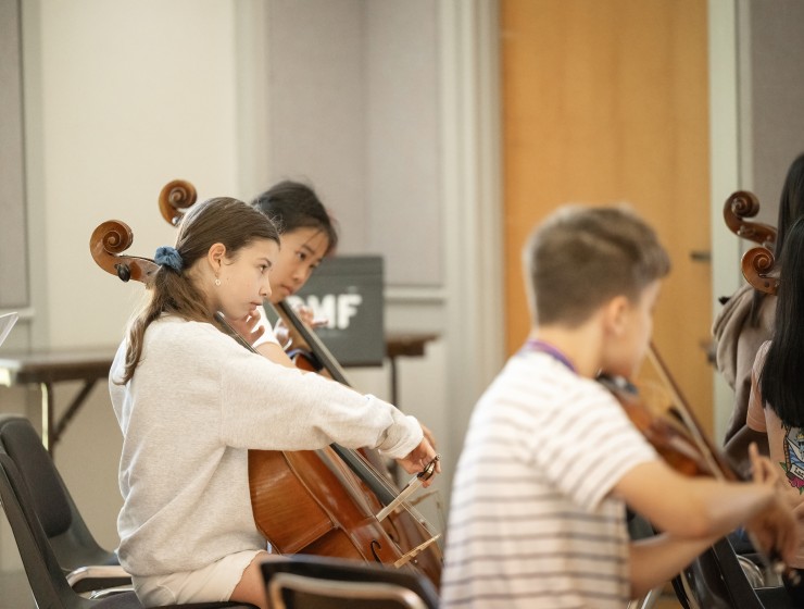 a cellist in the background plays, while a young violinist in the foreground is also playing
