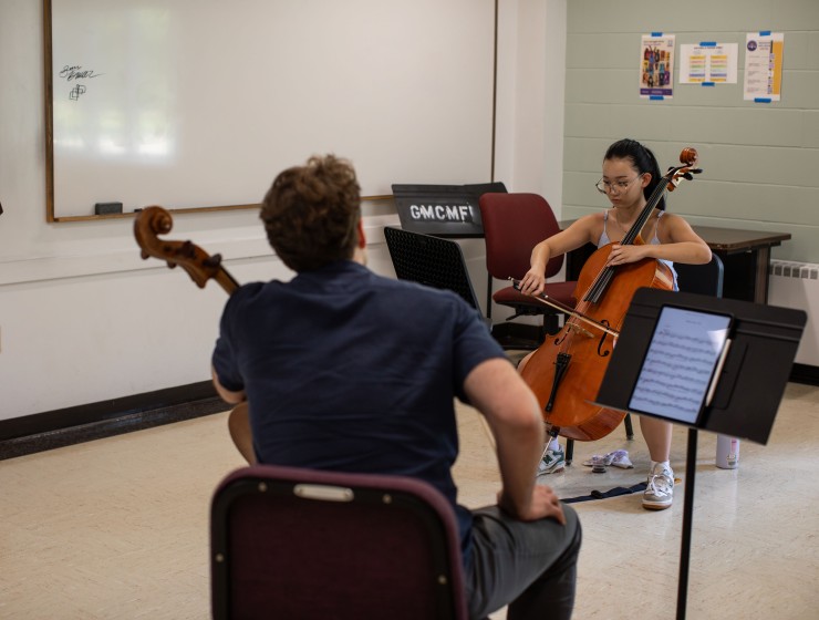A cello faculty member with their back to the camera teaching a cello student who is sitting in front of them