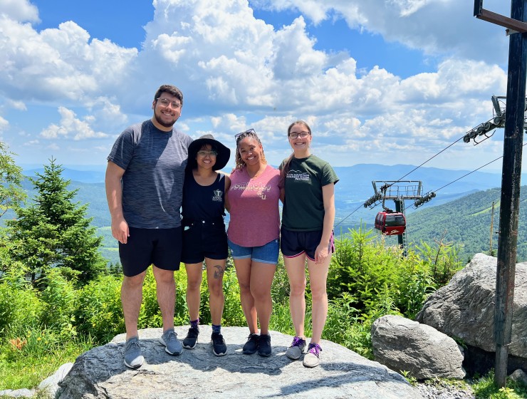 four students standing at the top of a vista with a mountain gondola in the background