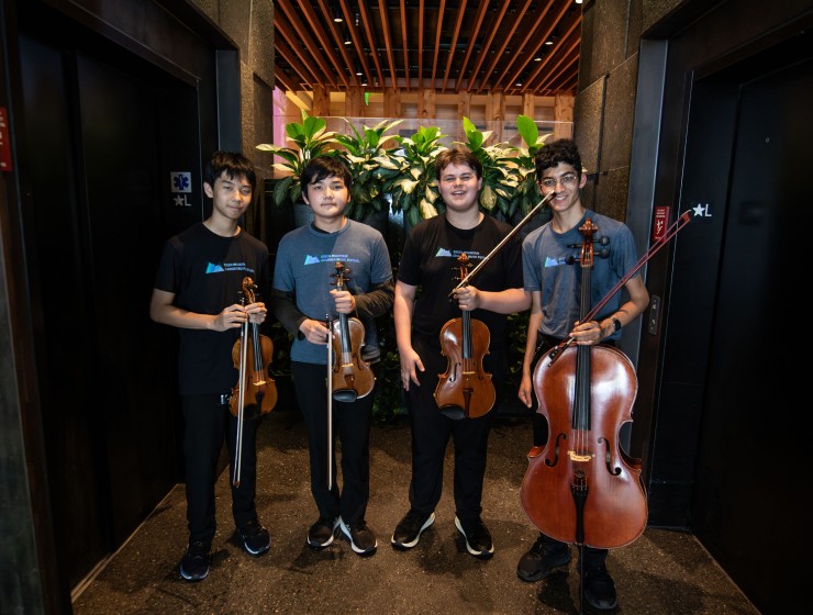 a group of students standing in an elevator lobby at a hotel holding their instruments