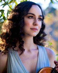 A woman with dark curly hair and a blue dress holding a violin