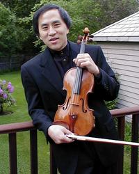 A violinist with a dark shirt standing on a deck holding a violin