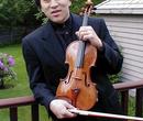 A violinist with a dark shirt standing on a deck holding a violin