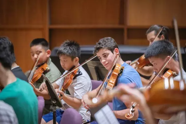 young violin students on stage playing in an orchestra; the image is focused on one student in the center of the bunch