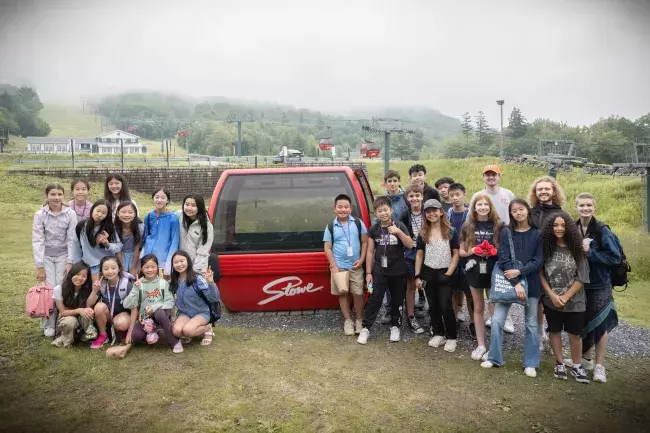a group of students standing around a red gondola car that says 'Stowe'