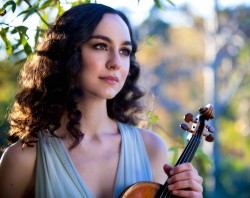 A woman with dark curly hair and a blue dress holding a violin