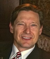 A close up photo of a man in a suit jacket with a white shirt and tie